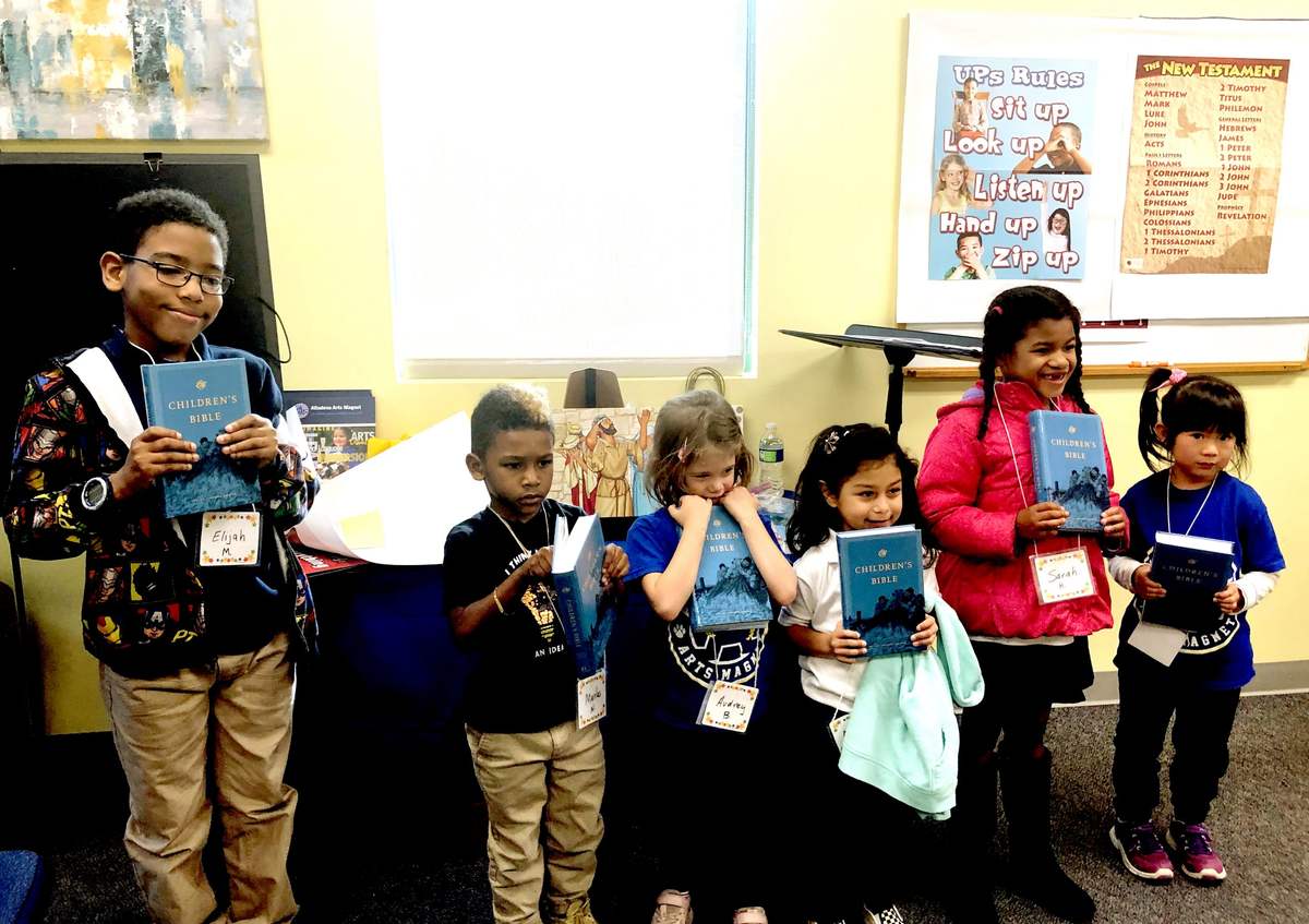 Children at a Good News Club standing together holding their new Bibles