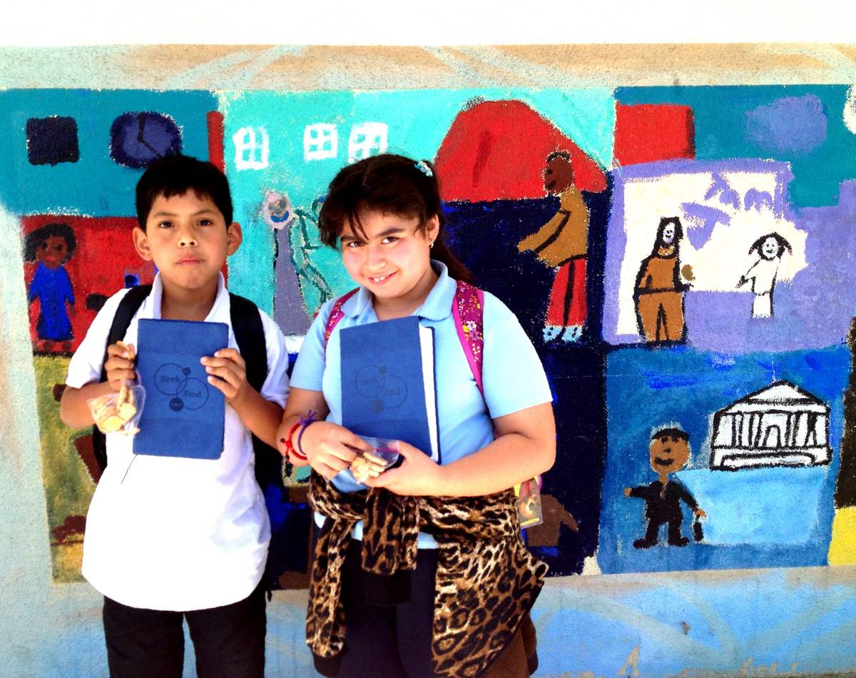 Two students holding Bibles in front of a colorful school mural